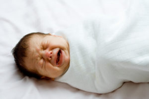 Newborn baby, wrapped in a white blanket, crying.