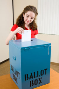 Young first time voter dropping her ballot in the box at the polling place.