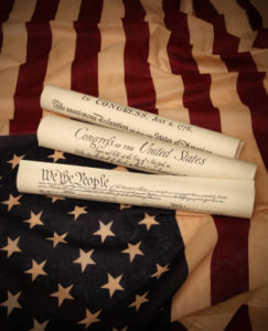 Documents of America History: Declaration of Independence, Bill of Rights and the US Constitution rolled up on top of an American flag
